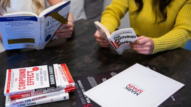 Two girls reading influential books for positive self-growth at Mark Spain Real Estate.