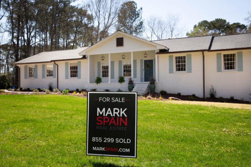 White brick home with great landscaping and for sale sign.